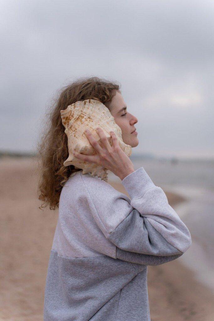 Mujer escuchando el sonido del caracol, en la playa